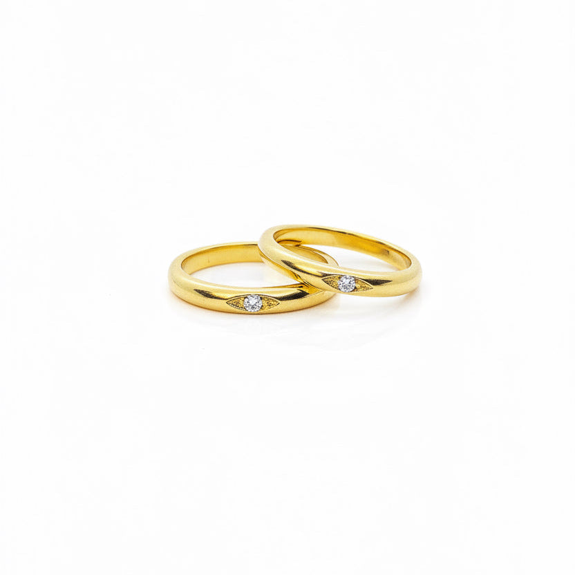  simple gold band ring with a round zirconia gemstone positioned in the center, displayed against a beige background.